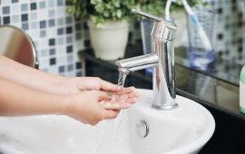 Crop shot of woman in bathroom washing hands in sink with clear stream of water